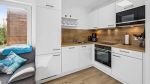 A modern kitchen with white cabinets, a wooden countertop, a built-in oven, and a black microwave.
