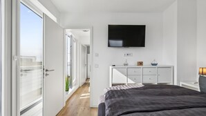 A bedroom with a bed, a TV mounted on the wall, a white dresser, and a balcony door.