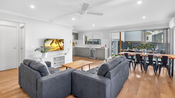 A modern living room with a grey sectional sofa, a wooden coffee table, and a dining area with a wooden table and black chairs.