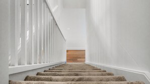 A staircase with white railings and carpeted steps leading to a landing with a small window.