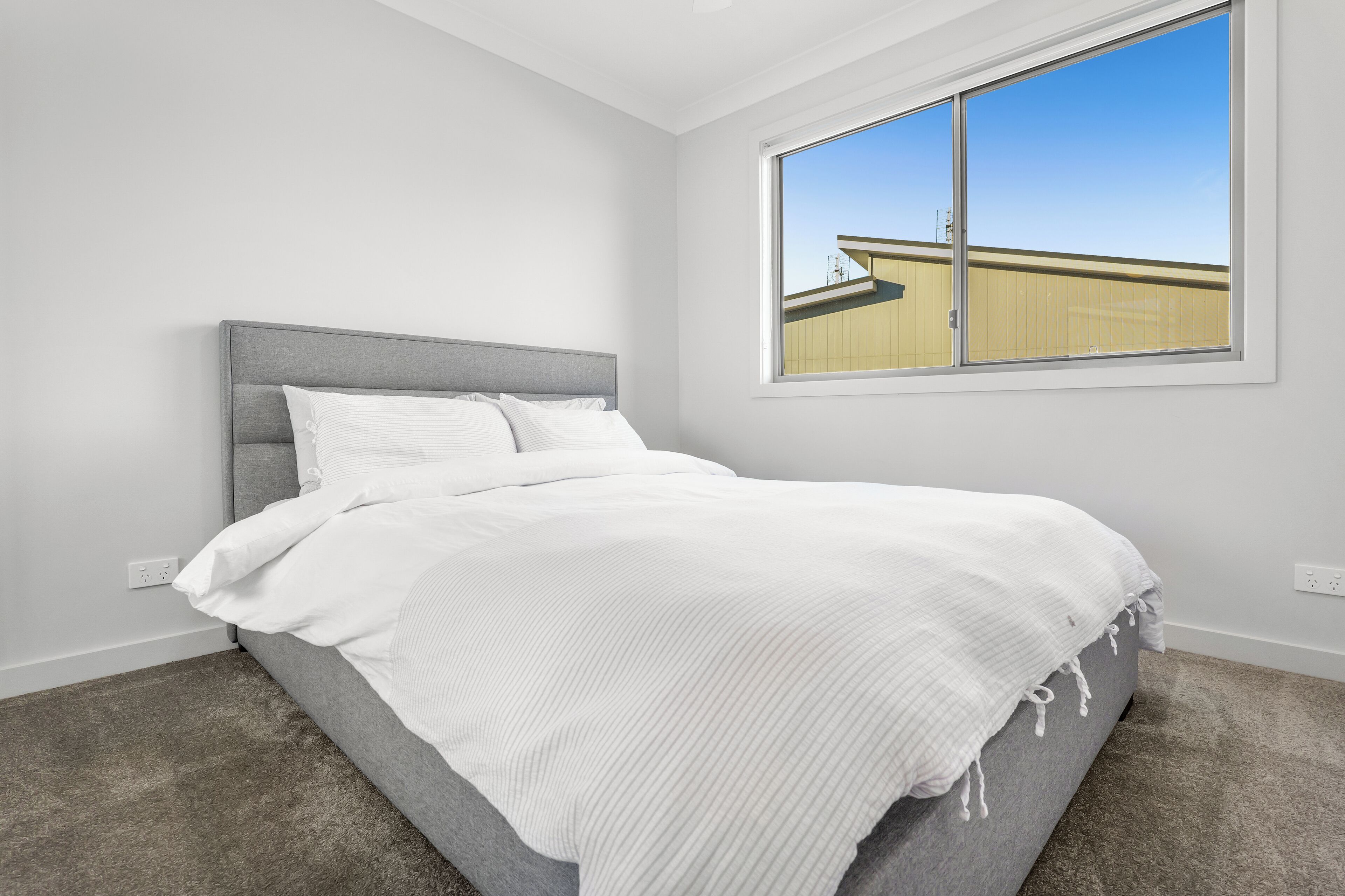 A bedroom with a bed, a window, and a carpeted floor.