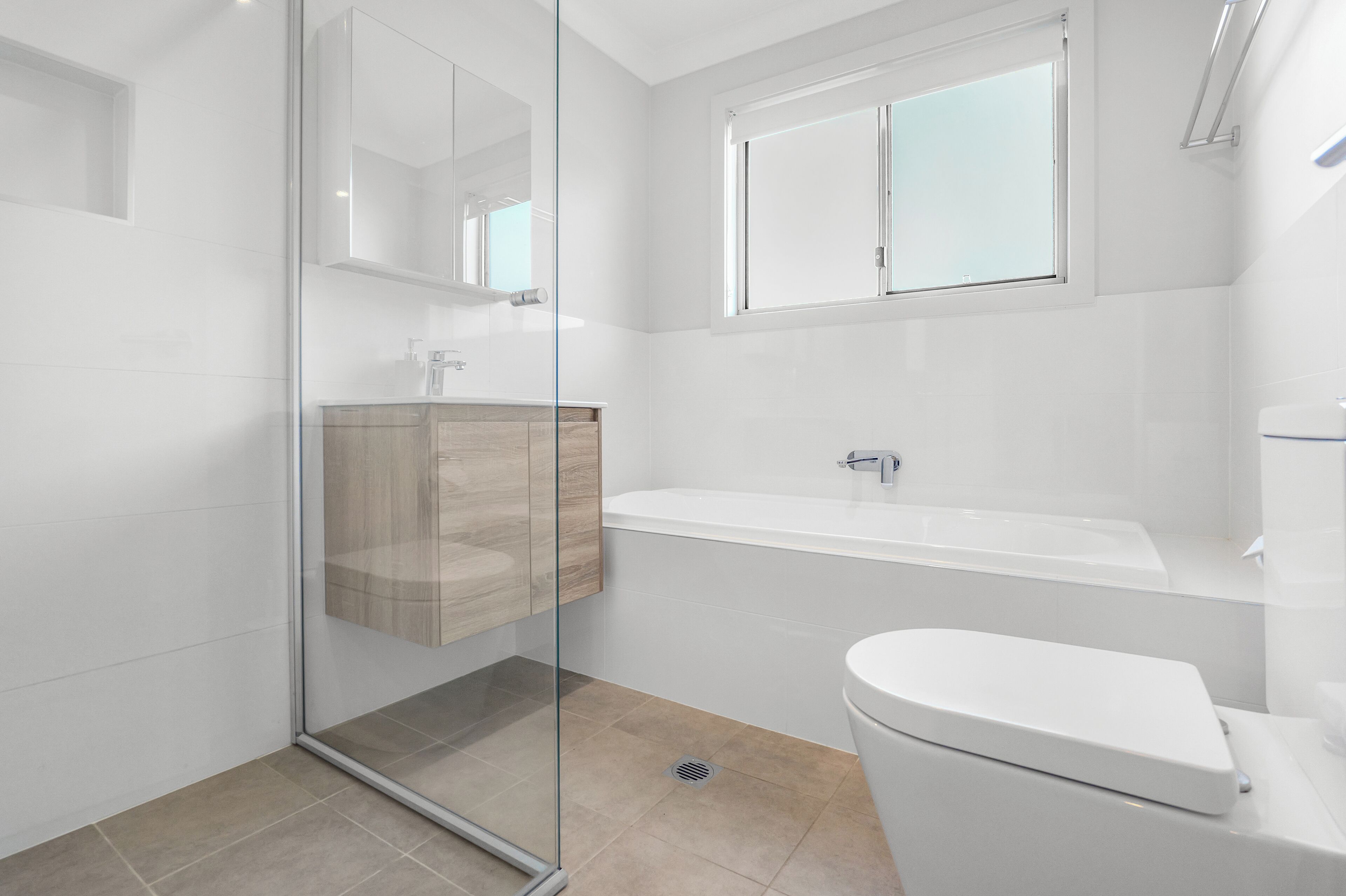 Un bany modern amb una dutxa tancada amb vidre, un moble de tocador de fusta, un lavabo blanc i un vàter.