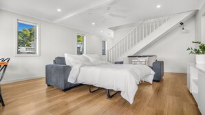 A modern bedroom with a bed, two sofas, a staircase, and a view of trees through the window.