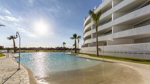 Um hotel moderno com piscina, palmeiras e céu claro.