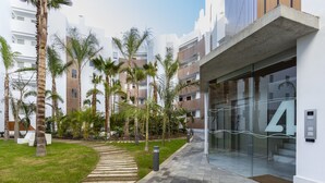 Um edifício moderno com entrada de vidro, cercado por palmeiras e um caminho pavimentado.