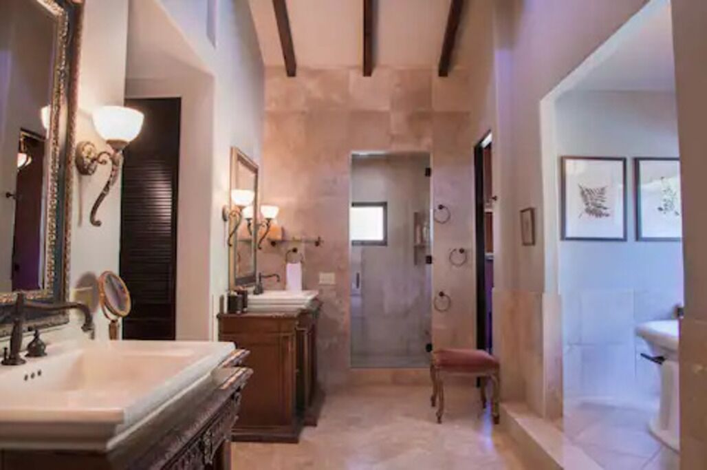 Une salle de bain avec un grand miroir, deux lavabos, une chaise et des œuvres d’art encadrées accrochées au mur.