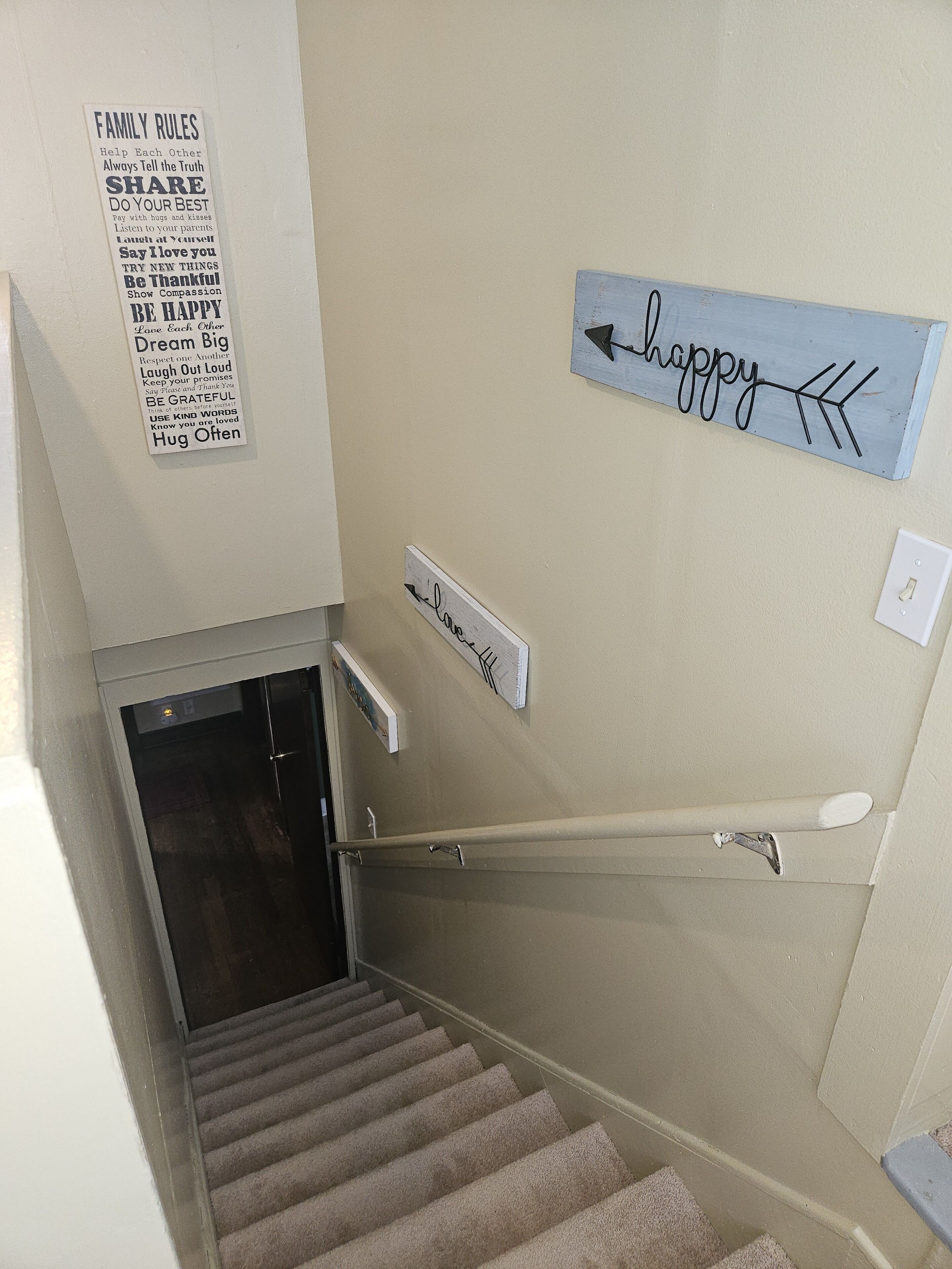 Una escalera con barandilla, un cartel en la pared con normas familiares y un letrero que dice 'feliz' con flechas.