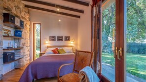 A bedroom with a bed, a chair, a shelf with books and decorative items, and a view of a garden through a glass door. - Lovely home in Rocca di Papa (Rocca di Papa)