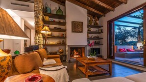 A cozy living room with a fireplace, wooden beams, stone wall, and a large window overlooking a garden. - Lovely home in Rocca di Papa (Rocca di Papa)