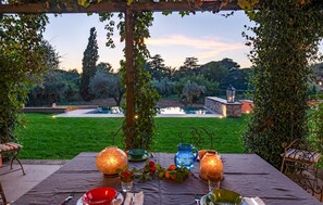 Un espacio de comedor al aire libre con una mesa lista para dos personas, rodeado de vegetación y vistas a un jardín y un estanque.