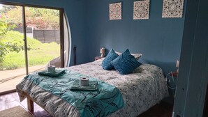 Ein Schlafzimmer mit Bett, Fenster, einer Wand mit dekorativen Paneelen und Blick auf Grün.