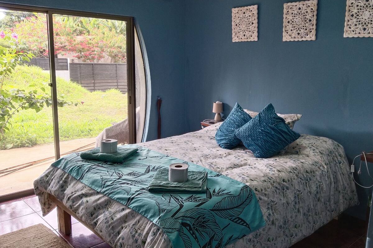 Une chambre à coucher avec un lit, une fenêtre, un mur orné de panneaux décoratifs et une vue sur la verdure à l’extérieur.