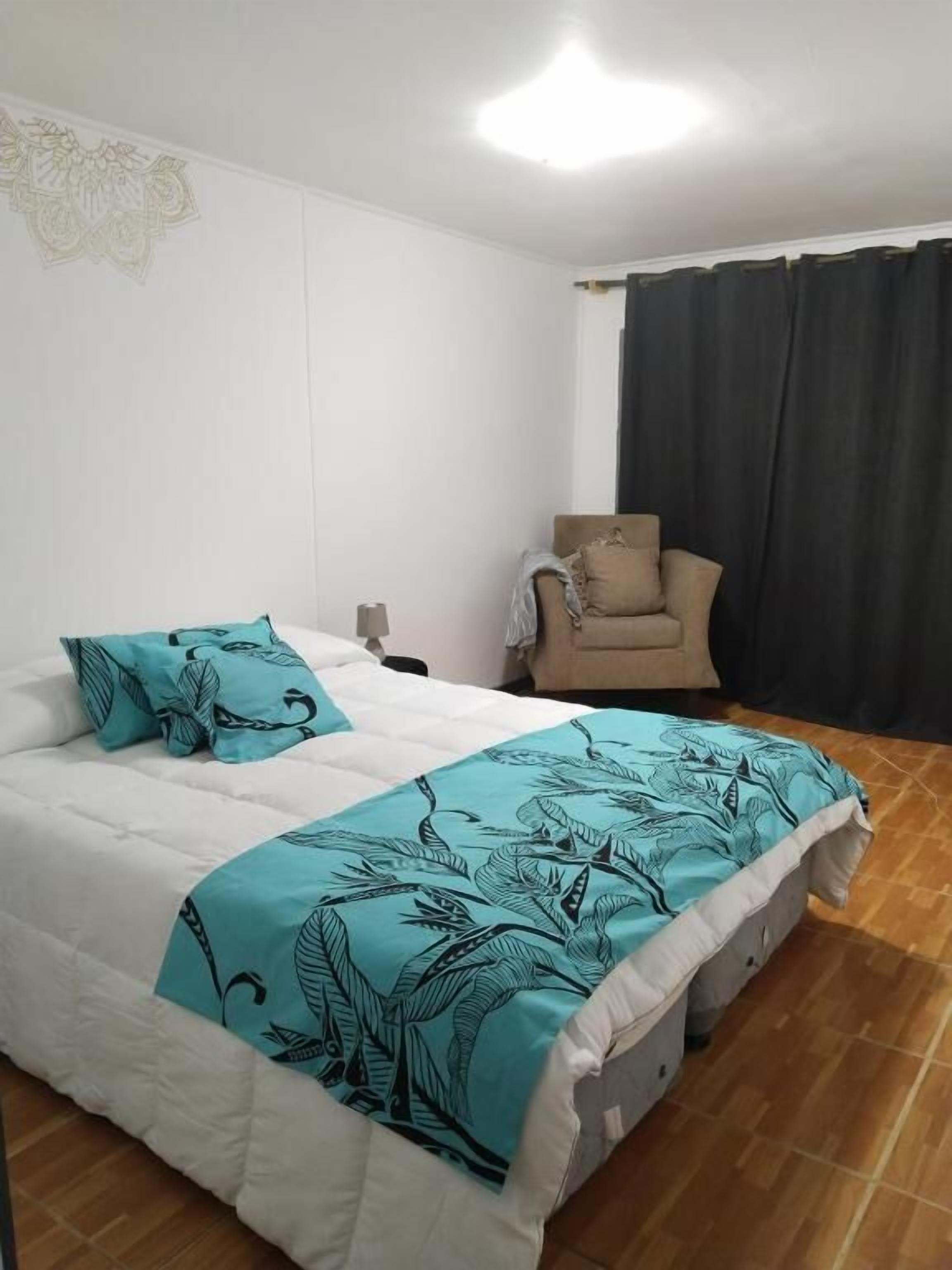 Un dormitorio con una cama, una silla, una mesita de noche y una ventana con cortinas.