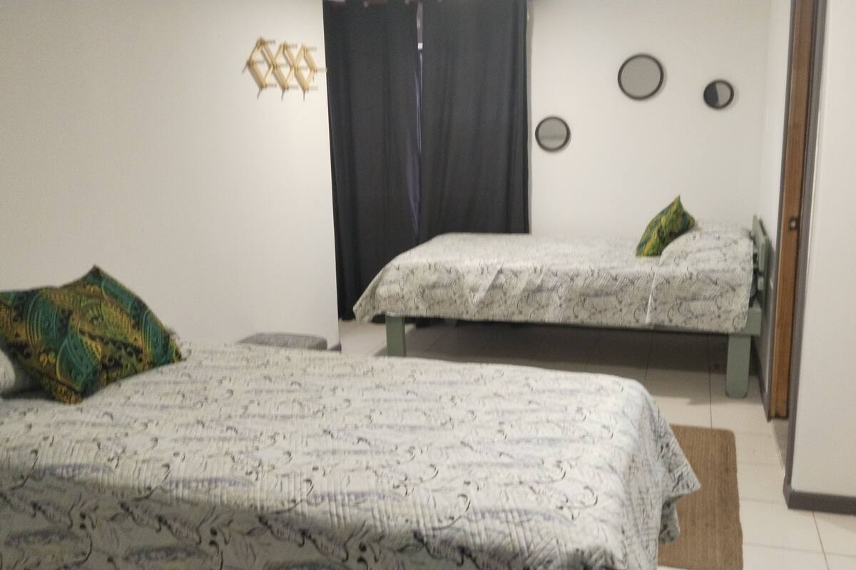 Une chambre avec deux lits, un rideau noir et une horloge fixée au mur.