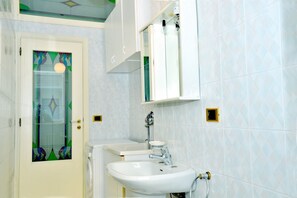Ein Badezimmer mit einem weißen Waschbecken, einer Glastür mit farbigem Dekor und einem Spiegel über dem Waschbecken sowie einer gefliesten Wand.
