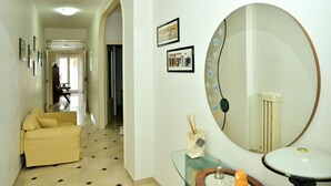 Camera d'albergo con divano, uno specchio rotondo, un tavolino con un vaso e quadri appesi al muro.