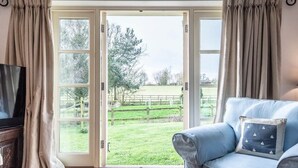 Una sala de estar con un sofá azul, un televisor y vistas a un campo verde a través de un ventanal.
