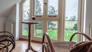 Una habitación con un ventanal grande, una mesa de madera con un vaso, y dos sillas de mimbre.