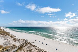 A beach with a clear sky, calm sea, and a sandy shore with beach chairs and umbrellas.