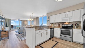 A modern kitchen with white cabinetry, a granite countertop, stainless steel appliances, and a view to the outside. - Gulf Views With Direct Beach Access! Terrace At Pelican Beach 1401! (Destin)
