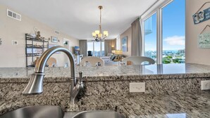 A modern kitchen with granite countertops, stainless steel fixtures, and a view of the city through large windows. - Gulf Views With Direct Beach Access! Terrace At Pelican Beach 1401! (Destin)