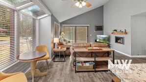 A modern living room with a ceiling fan, a fireplace, a TV, and a dining area with a table and chairs. - Twin Lakes Village Home—Golf Retreat, Community Pool, Corner Lot, and Single-Level Living! (Rathdrum)