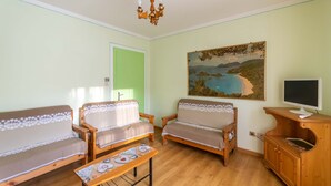 A living room with two wooden sofas, a wooden coffee table, a painting on the wall, and a television on a wooden stand. - Casa Iris 2 (Falcade)