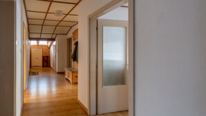Un couloir doté d’un plancher en bois, d’une porte avec un panneau en verre dépoli et d’un plafond avec des poutres en bois.