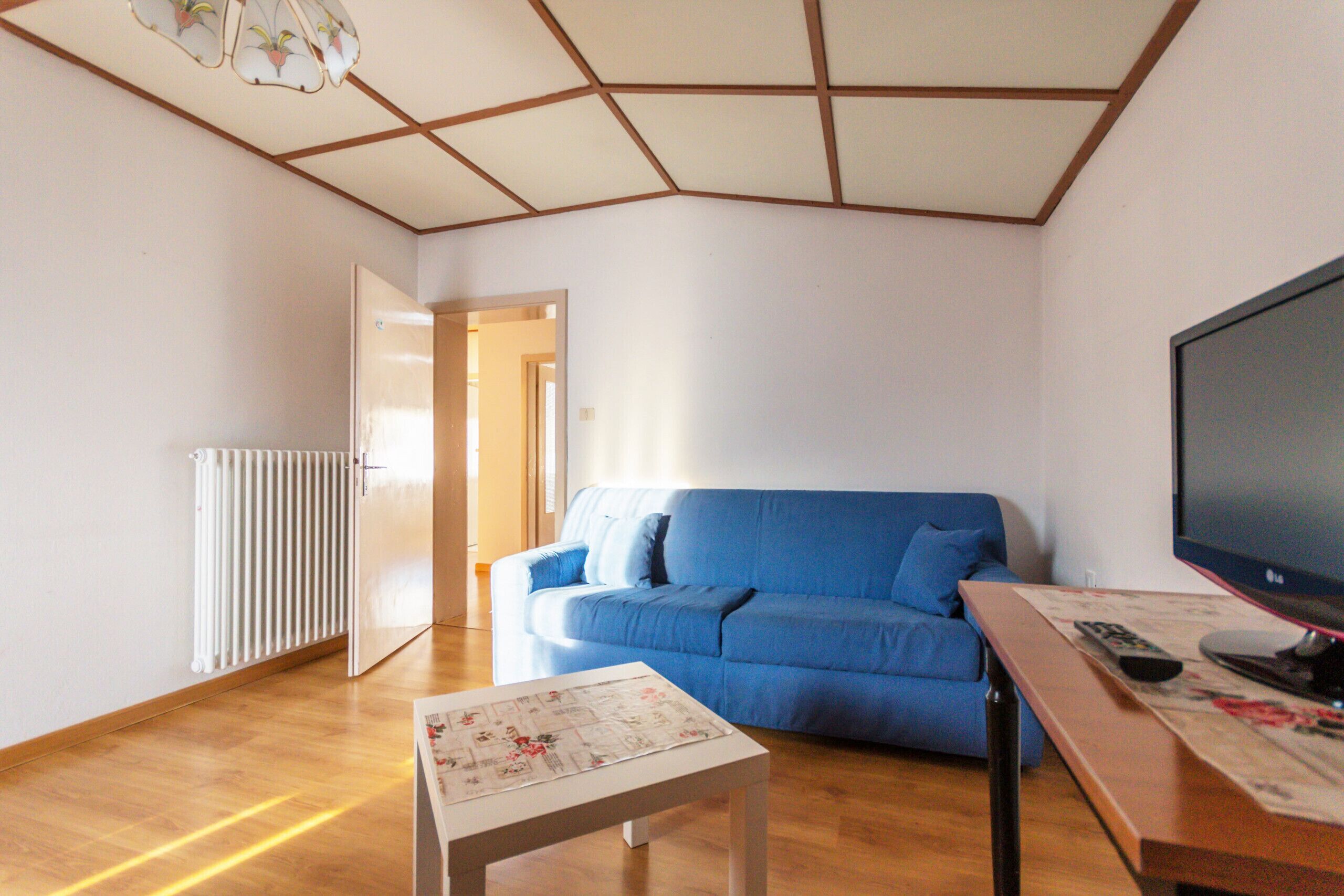 Un salon avec un canapé bleu, une table basse en bois, un téléviseur posé sur un meuble et un radiateur fixé au mur.