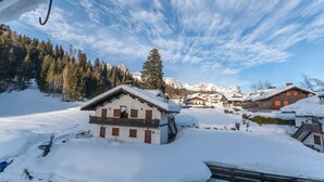 Un village enneigé, avec ses maisons traditionnelles en bois, un paysage montagneux en toile de fond et un ciel dégagé.