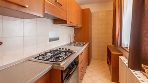 Une cuisine avec des meubles de rangement en bois, une cuisinière à gaz, un évier et une fenêtre avec des rideaux.