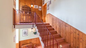 A wooden staircase with a railing, leading to a landing with a wooden cabinet and wall-mounted lights.