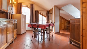A dining area with a table and chairs, wooden cabinets, a refrigerator, and a window with curtains.