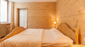 A wooden-paneled room with a bed, a chair, and a window. - Villa Licia bilo (Falcade)