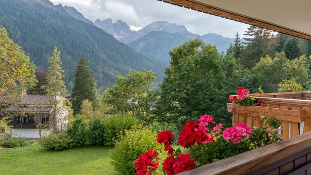 A balcony with a view of a mountainous landscape, a wooden deck, and red flowers. - Villa Licia trilo (Falcade)