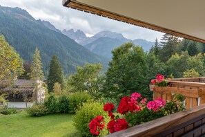Un balcón con vistas a un paisaje montañoso, una terraza de madera y flores rojas.