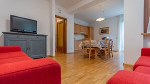 A living room with red sofas, a TV on a grey cabinet, and a wooden dining table with chairs. - Villa Licia trilo (Falcade)