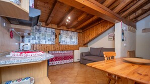 A cozy kitchen with wooden beams, a dining table, and a sofa. - Casa Falcade 10 (Falcade)