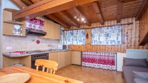 A kitchen with wooden beams, a dining table, and a sofa. - Casa Falcade 10 (Falcade)