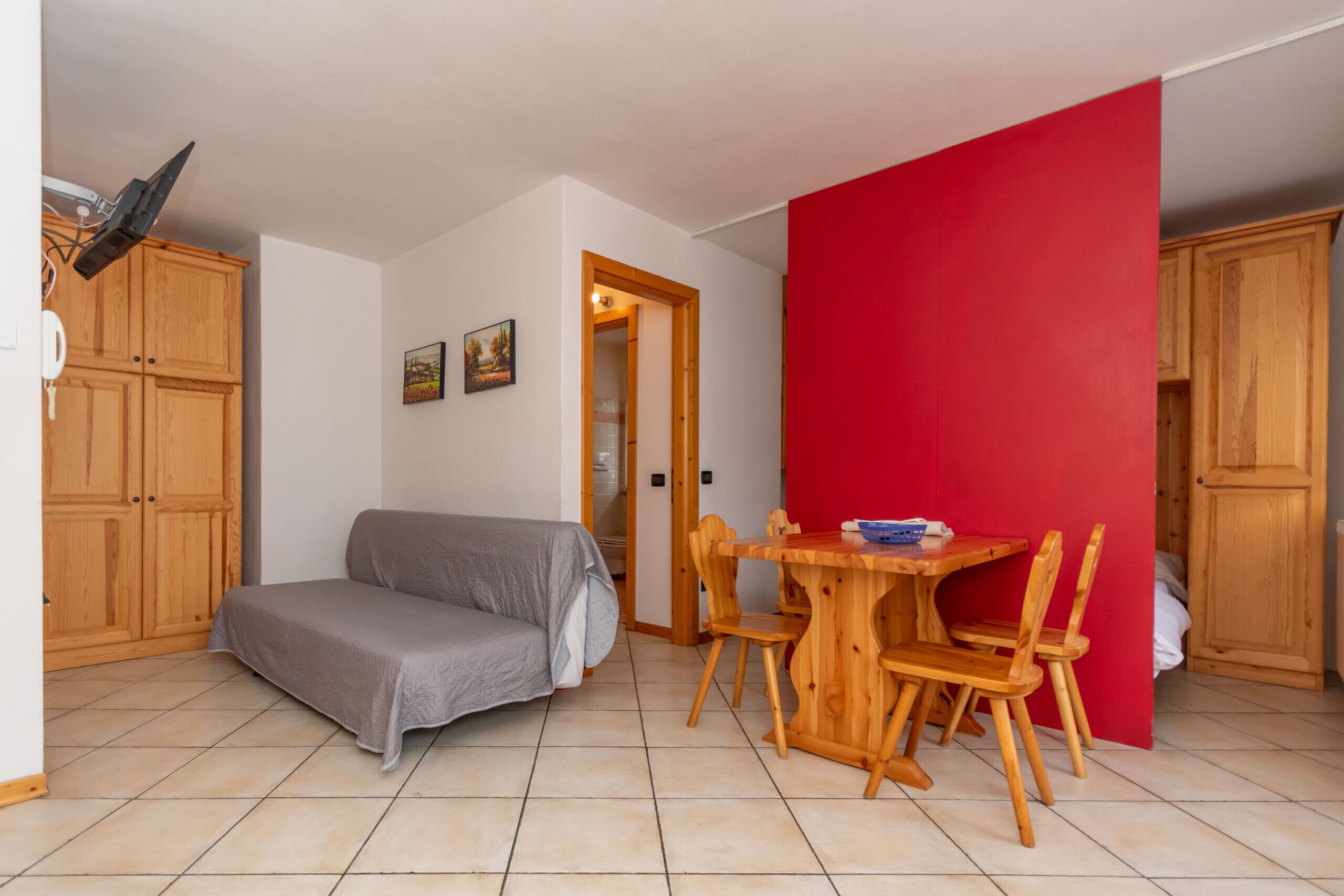 Un espai habitable compacte amb un sofà, una taula de dinar i caires, i armaris de fusta.