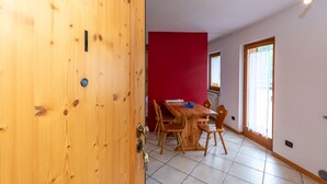 A wooden door with a keyhole, a red wall, a wooden dining table with chairs, and a window with curtains.