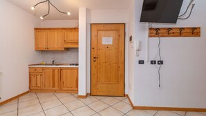 A kitchen with wooden cabinets, a tiled floor, a door with a notice, a mounted TV, and a wall-mounted phone.