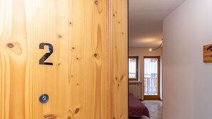 A wooden door with the number 2, a room with a bed and a window, and a balcony with a railing.