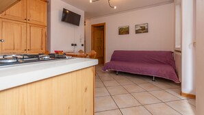 A compact kitchen with wooden cabinets, a built-in gas stove, and a flat-screen TV mounted on the wall.