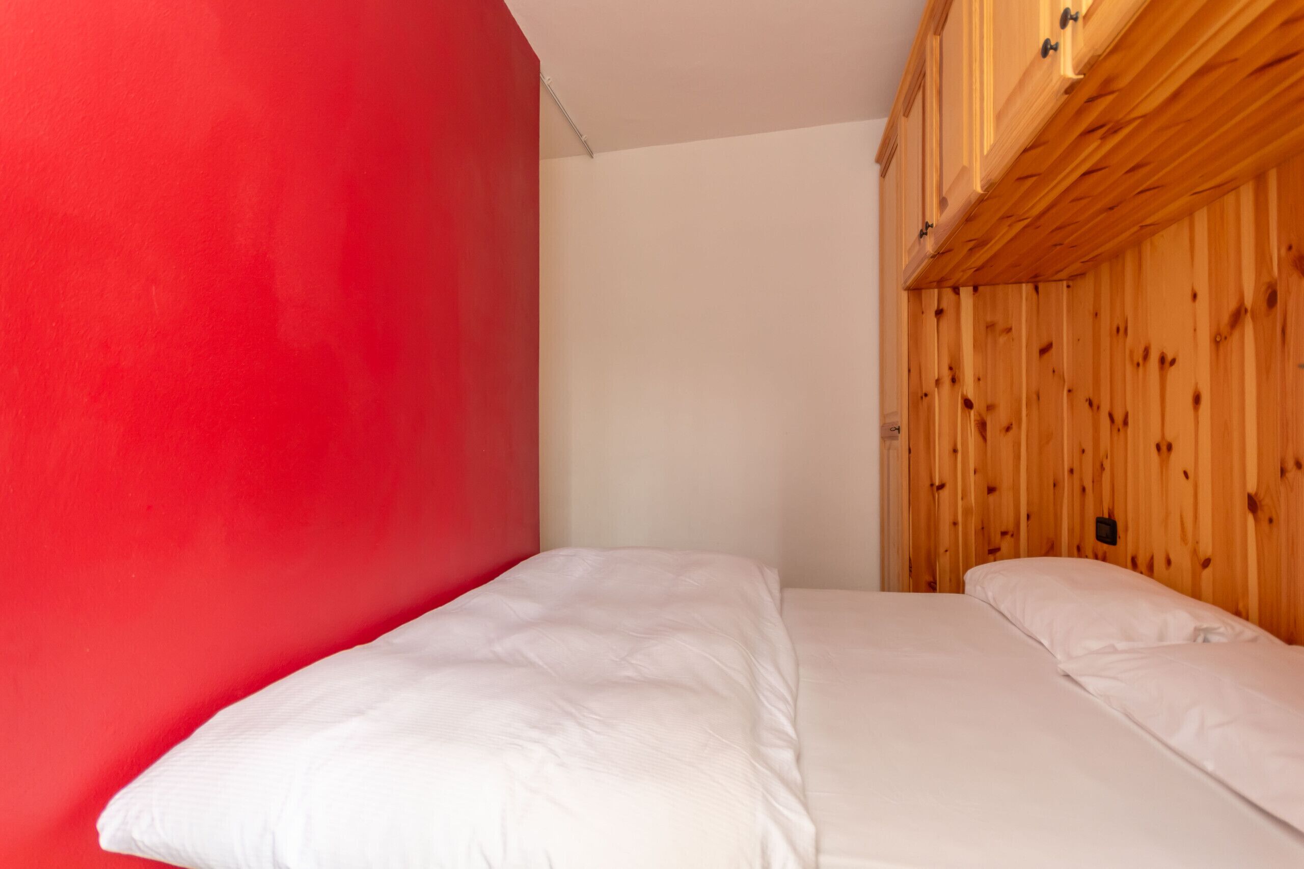 A room with a bed, a red wall, and wooden paneling.