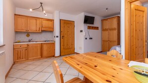Une cuisine avec des meubles en bois, une table à manger et un téléviseur fixé au mur.