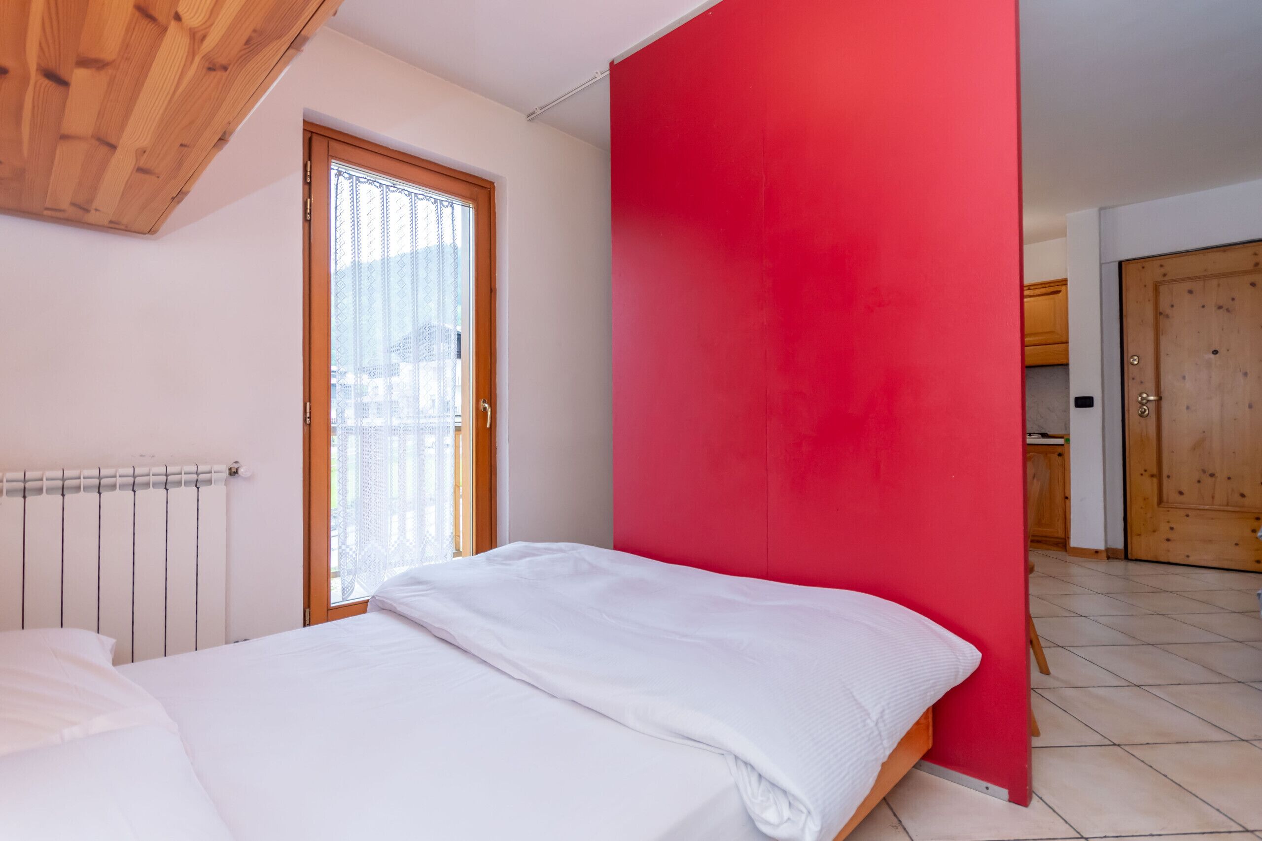 Een slaapkamer met een bed, een raam, een rode muur en een houten plafond.