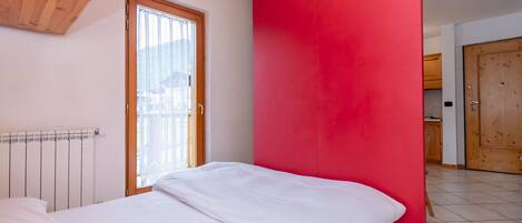 Een slaapkamer met een bed, een raam, een rode muur en een houten plafond.