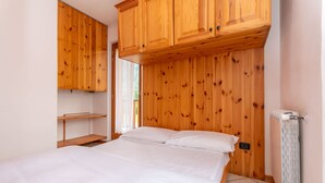 Une chambre à coucher avec une tête de lit en bois, un lit recouvert de draps blancs, une armoire en bois et un radiateur.
