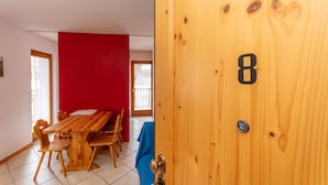 A wooden door with the number 8, a wooden dining table with chairs, and a red wall. - Casa Stella 8 (Falcade)